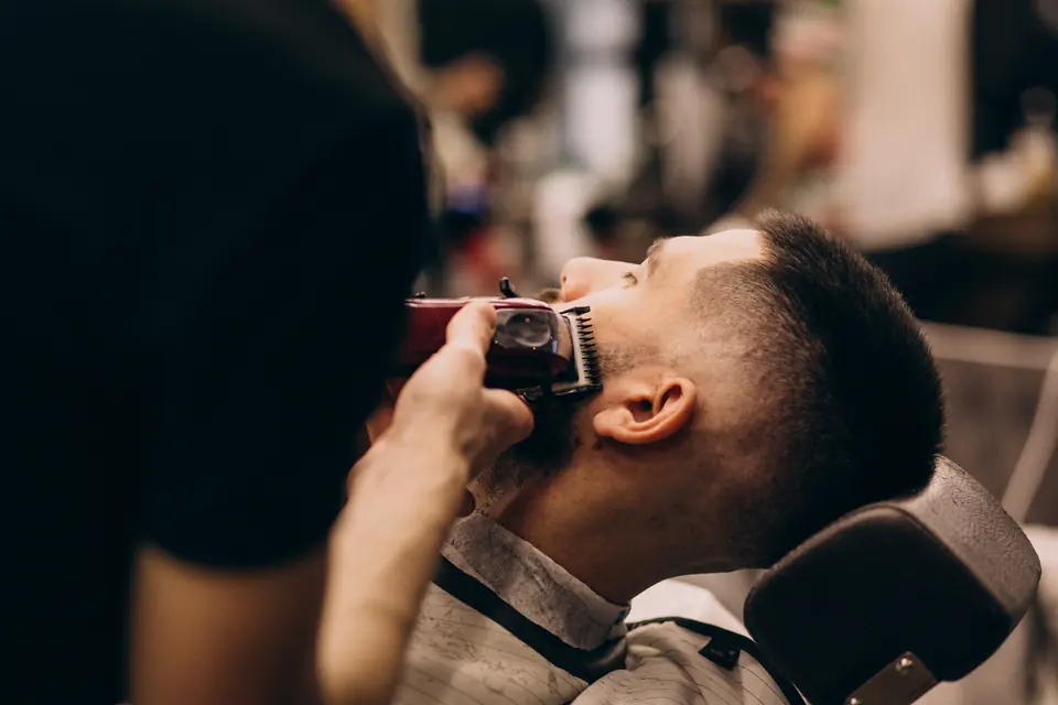 Barbeiro aparando a barba do cliente com máquina