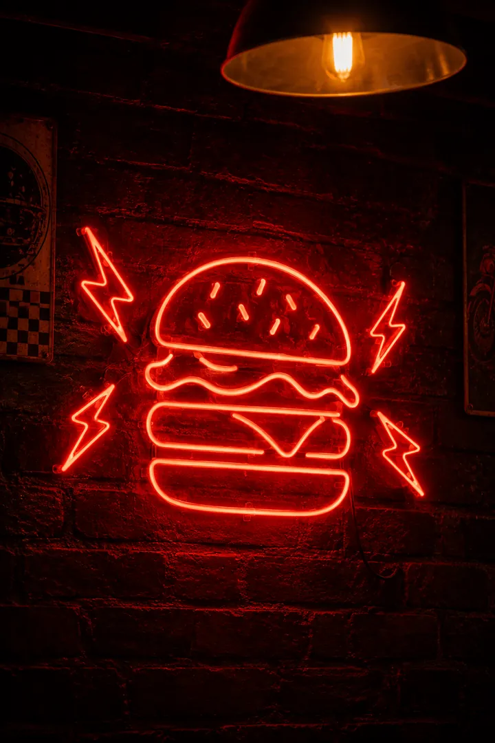 Letreiro neon vermelho em forma de hambúrguer com raios, na parede de tijolos