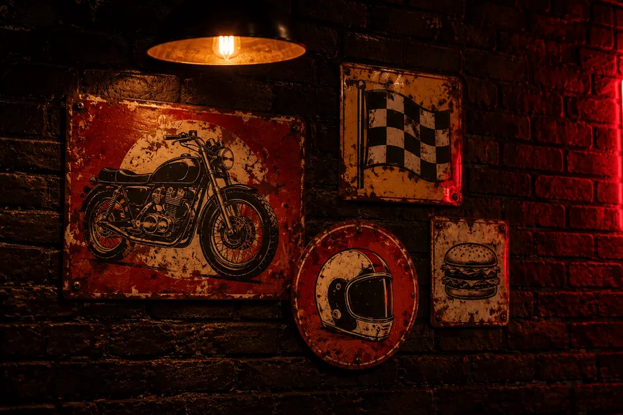 Placas retrô de metal na parede de tijolos: uma moto, uma bandeira quadriculada, um capacete e um hambúrguer